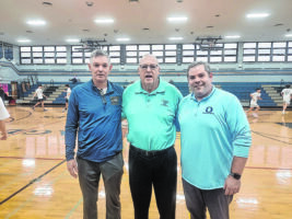 Three basketball coaches standing side by side in an empty gymnasium. All three are wearing blue shirts.